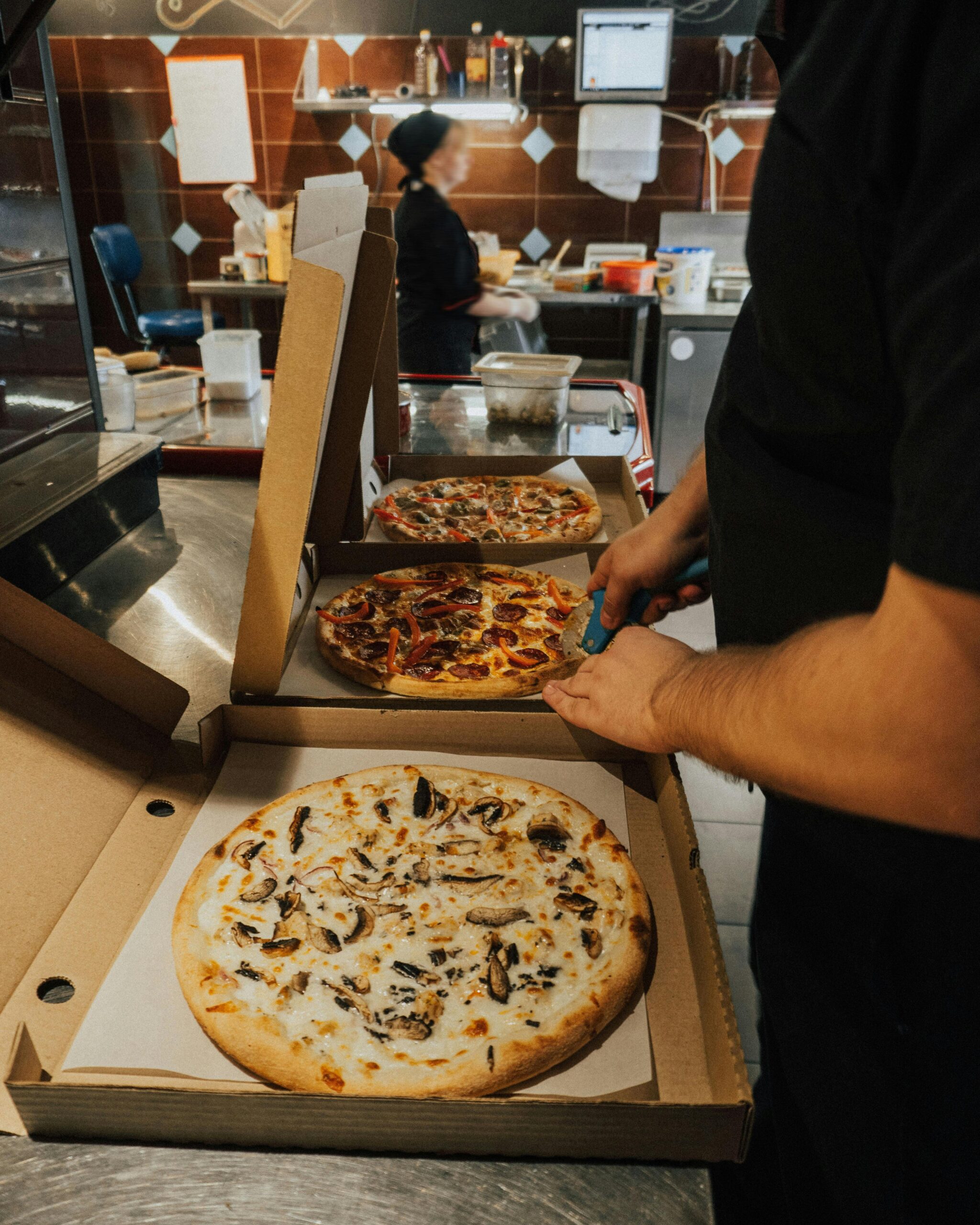 Person cutting pizza slices from multiple pizza boxes.