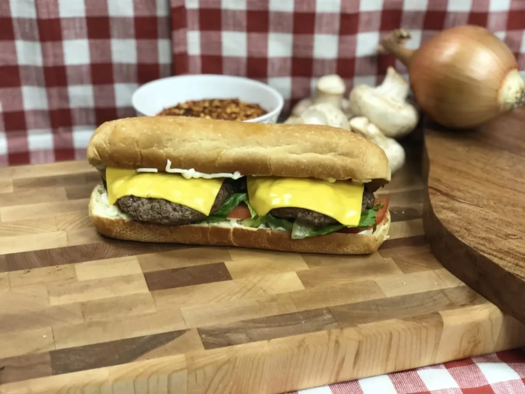 Cheeseburger sub with two grilled beef patties, melted American cheese, lettuce, and tomato on a hoagie roll.