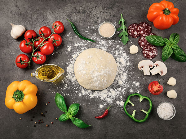 A ball of pizza dough with yeast in pizza dough A ball of pizza dough with yeast in pizza dough, surrounded by various pizza toppings like tomatoes, peppers, mushrooms, herbs, and spices.