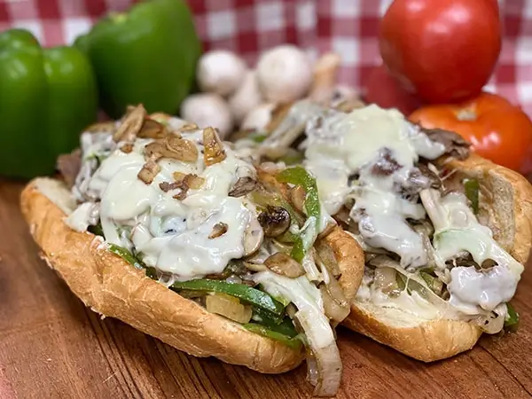 Two Philly cheesesteak subs loaded with grilled onions, green peppers, mushrooms, and melted provolone cheese.