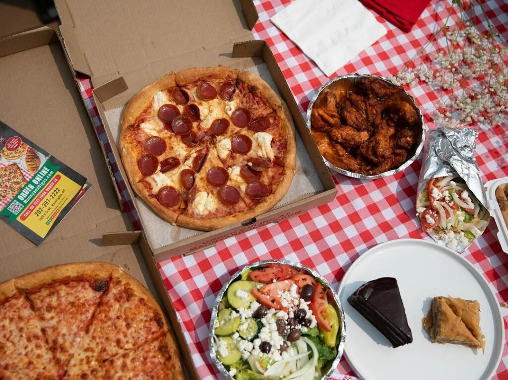 Pizza, chicken wings, and wraps from Manny & Olga’s served on a checkered tablecloth.