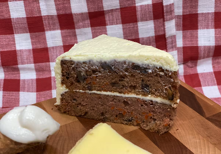 A catering presentation of a slice of layered carrot cake with cream cheese frosting, set on a wooden surface.