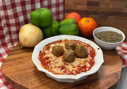 A catering presentation of a dish featuring meatballs in marinara sauce, topped with melted cheese and served in a white dish.