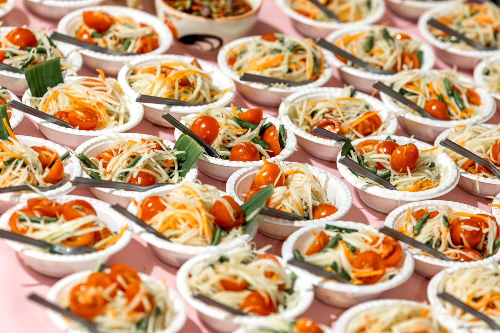 A catering platter A catering platter filled with small bowls of fresh papaya salad, each garnished with a cherry tomato.