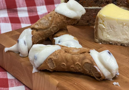 cannoli filled with creamy ricotta A catering presentation of three cannoli filled with creamy ricotta and chocolate chips, arranged on a wooden surface.
