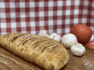 Golden baked calzone on a wooden board with mushrooms and tomatoes.
