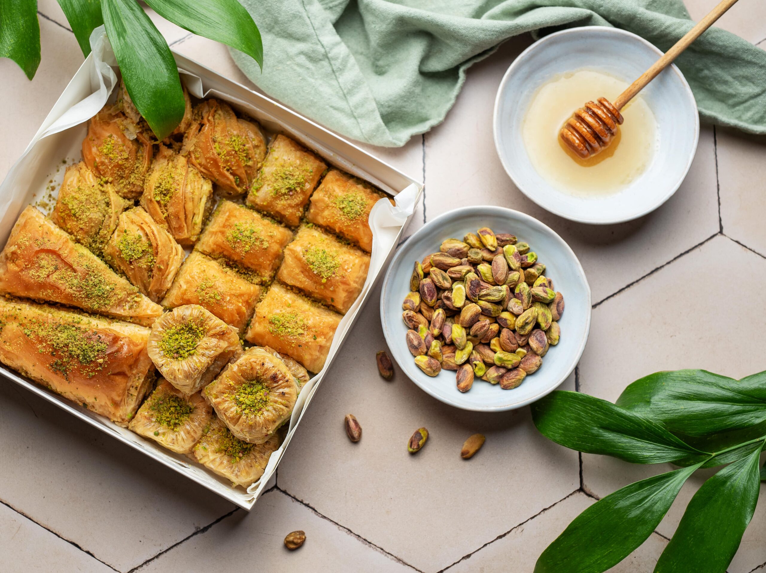 A box of assorted baklava pieces A box of assorted baklava pieces, including triangular, rolled, and square shapes, garnished with crushed pistachios.