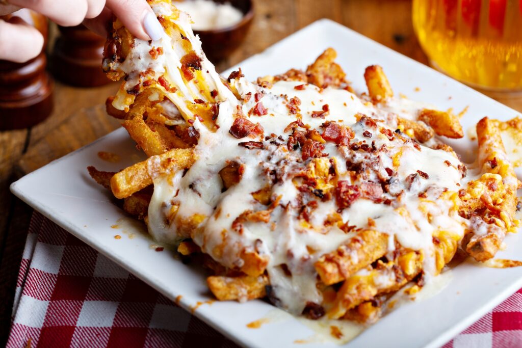 Cheesy fries loaded with bacon served on a white plate on a red checkered tablecloth.