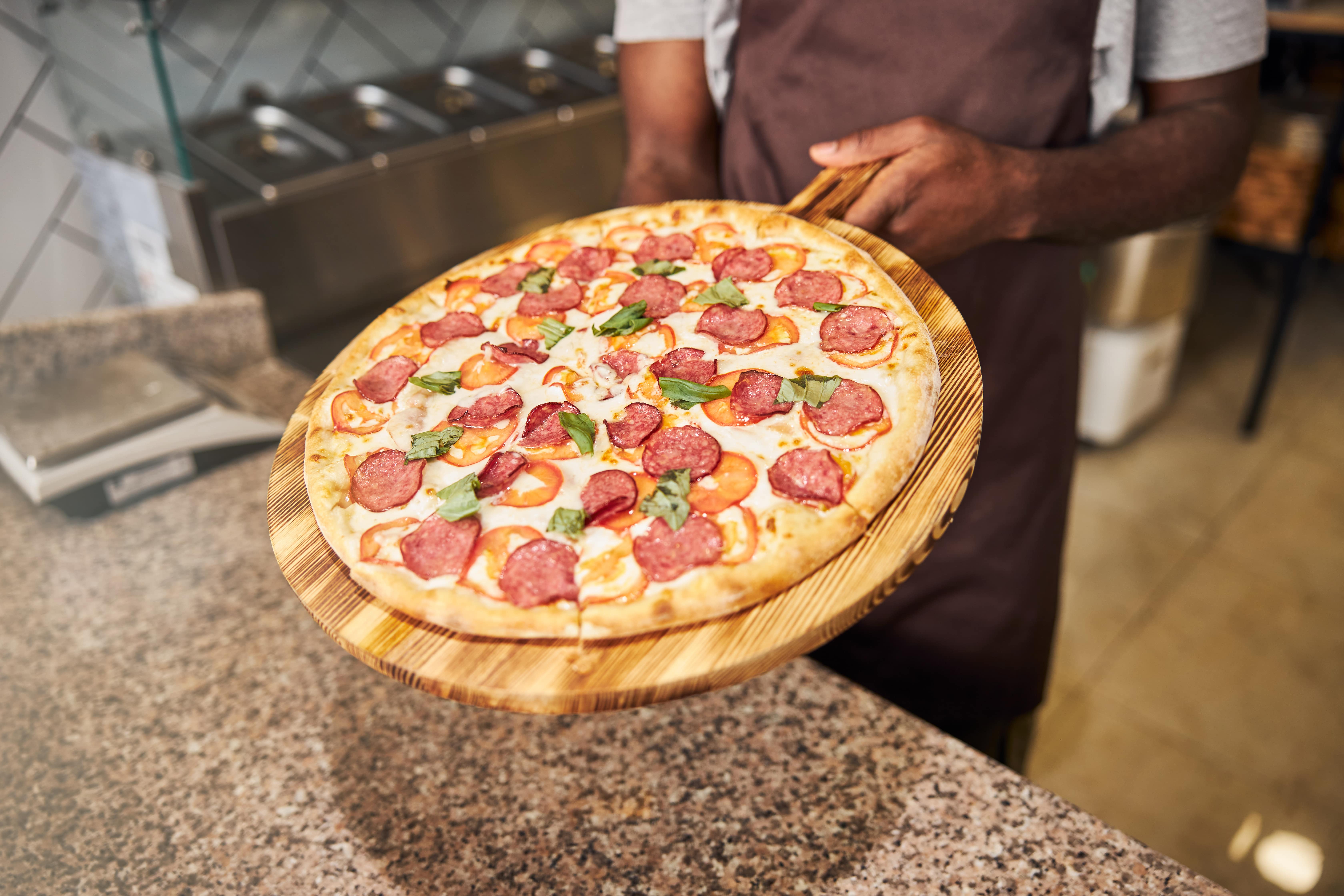 A freshly made pepperoni pizza topped with basil leaves being served on a wooden pizza peel, ready for a pizza party.
