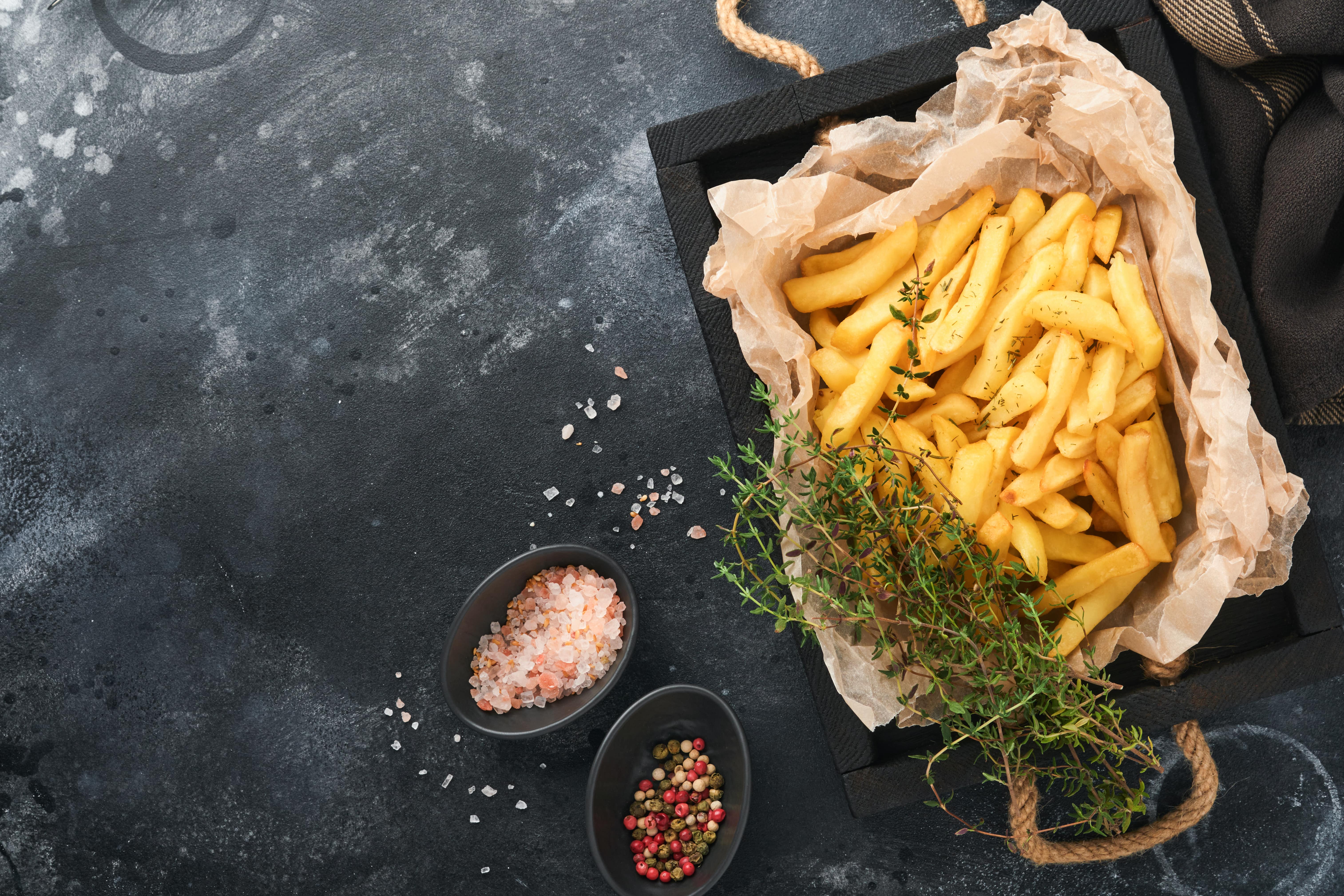 A rustic serving of cheesy fries with herbs, pink salt, and spices on a dark textured surface.