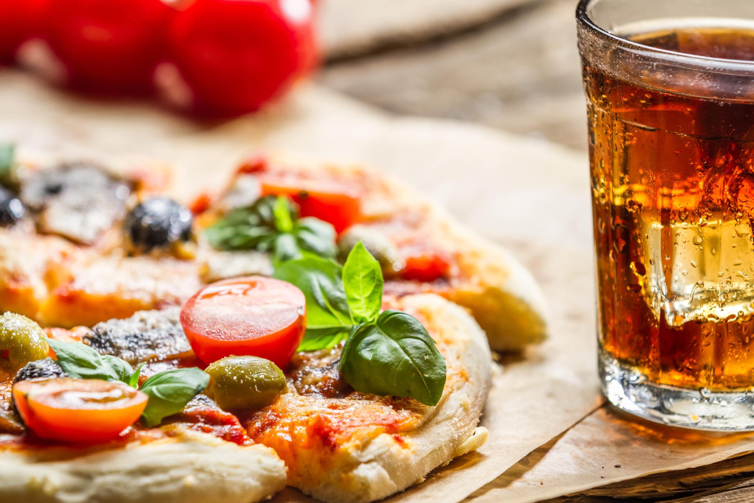 Close-up of a meat lovers pizza Close-up of a meat lovers pizza topped with fresh basil, cherry tomatoes, olives, and melted cheese, paired with a refreshing glass of cola.