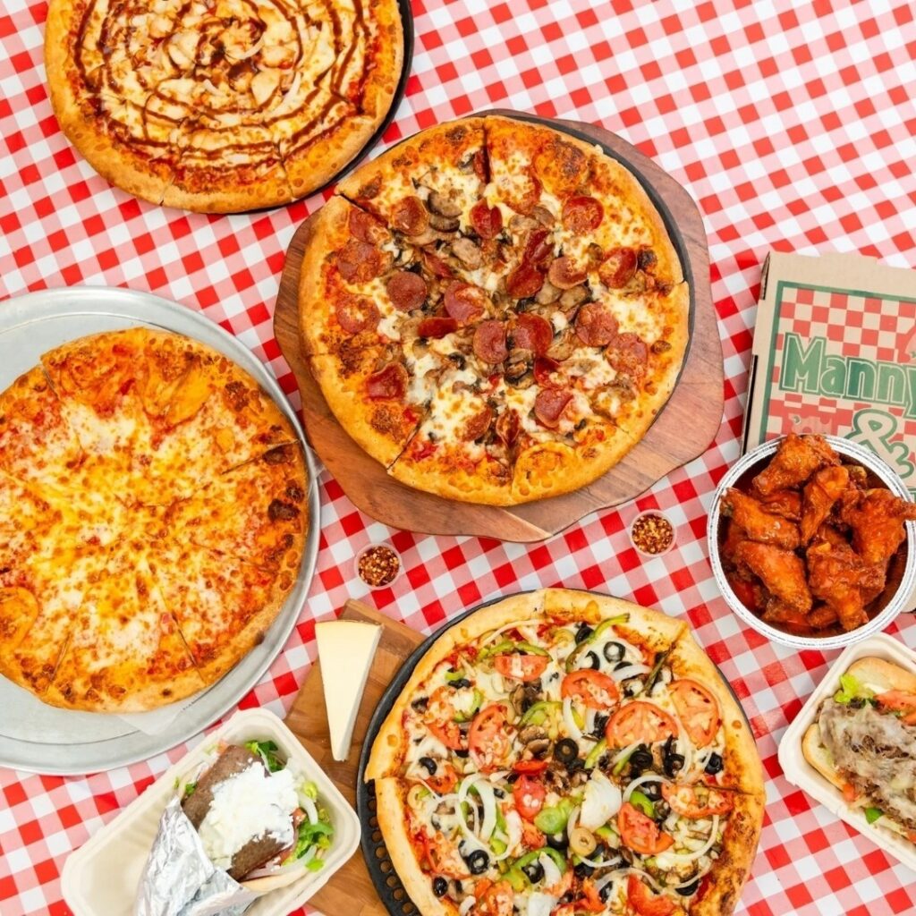 Assorted pizzas, wings, and subs arranged as a full corporate catering spread from Manny & Olga’s.