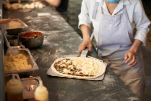 A person in an apron preparing pizza at a floured counter, like at Manny & Olga’s kitchen.