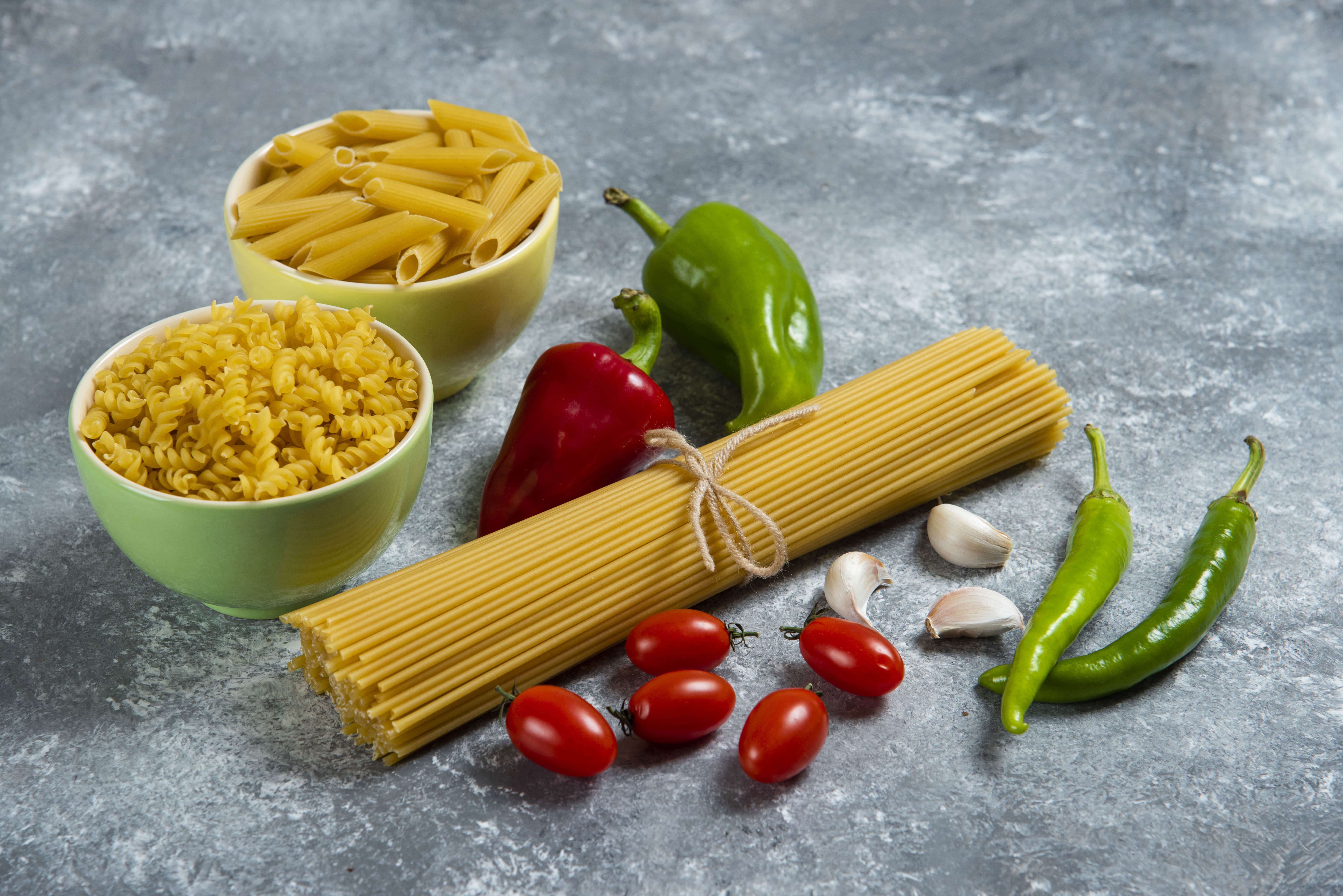 An artistic display of raw pasta and fresh vegetables, ideal for creating a hearty Italian dish.
