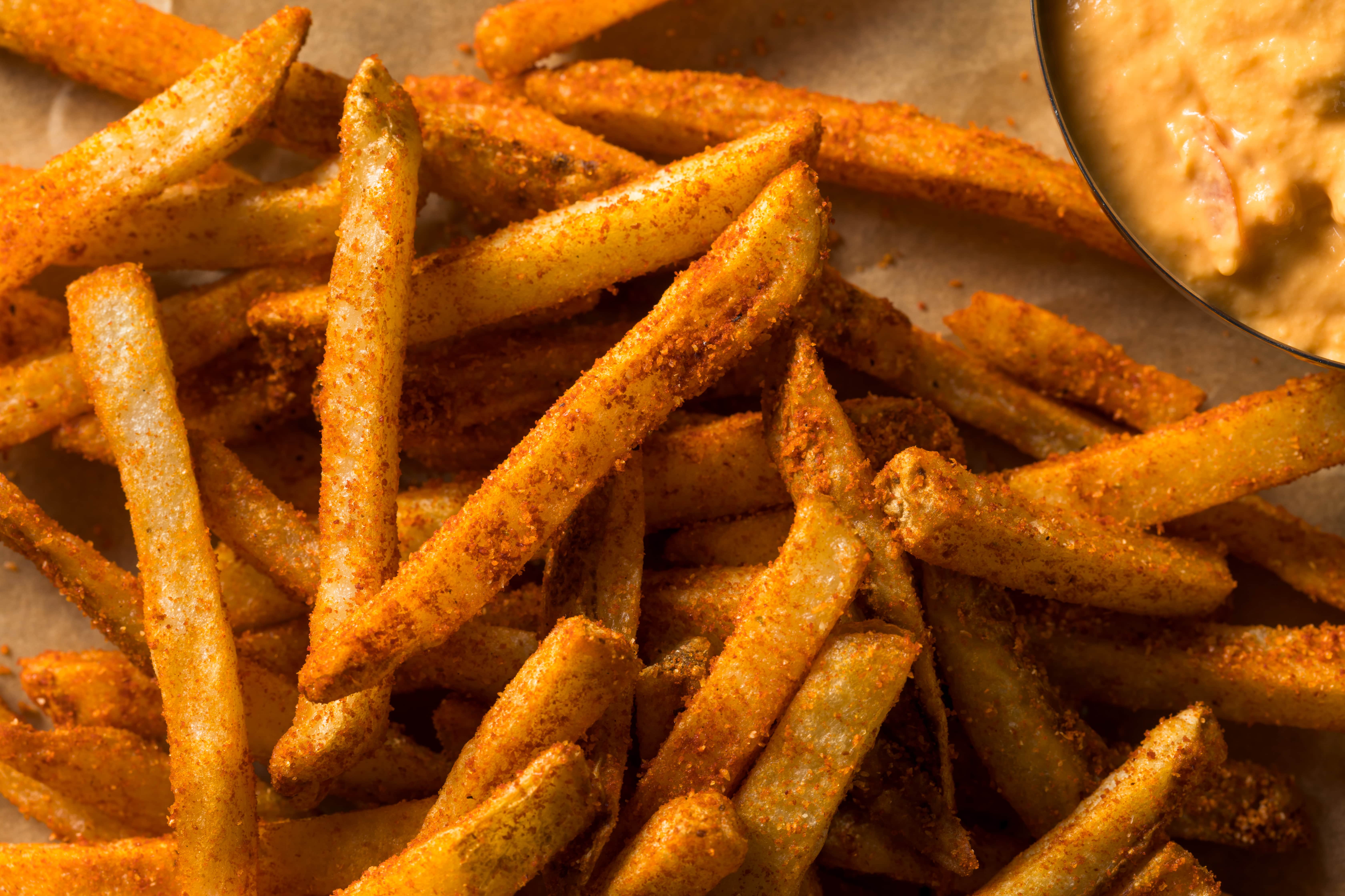 A pile of crispy, golden French fries dusted with spices, served with a side of dipping sauce.