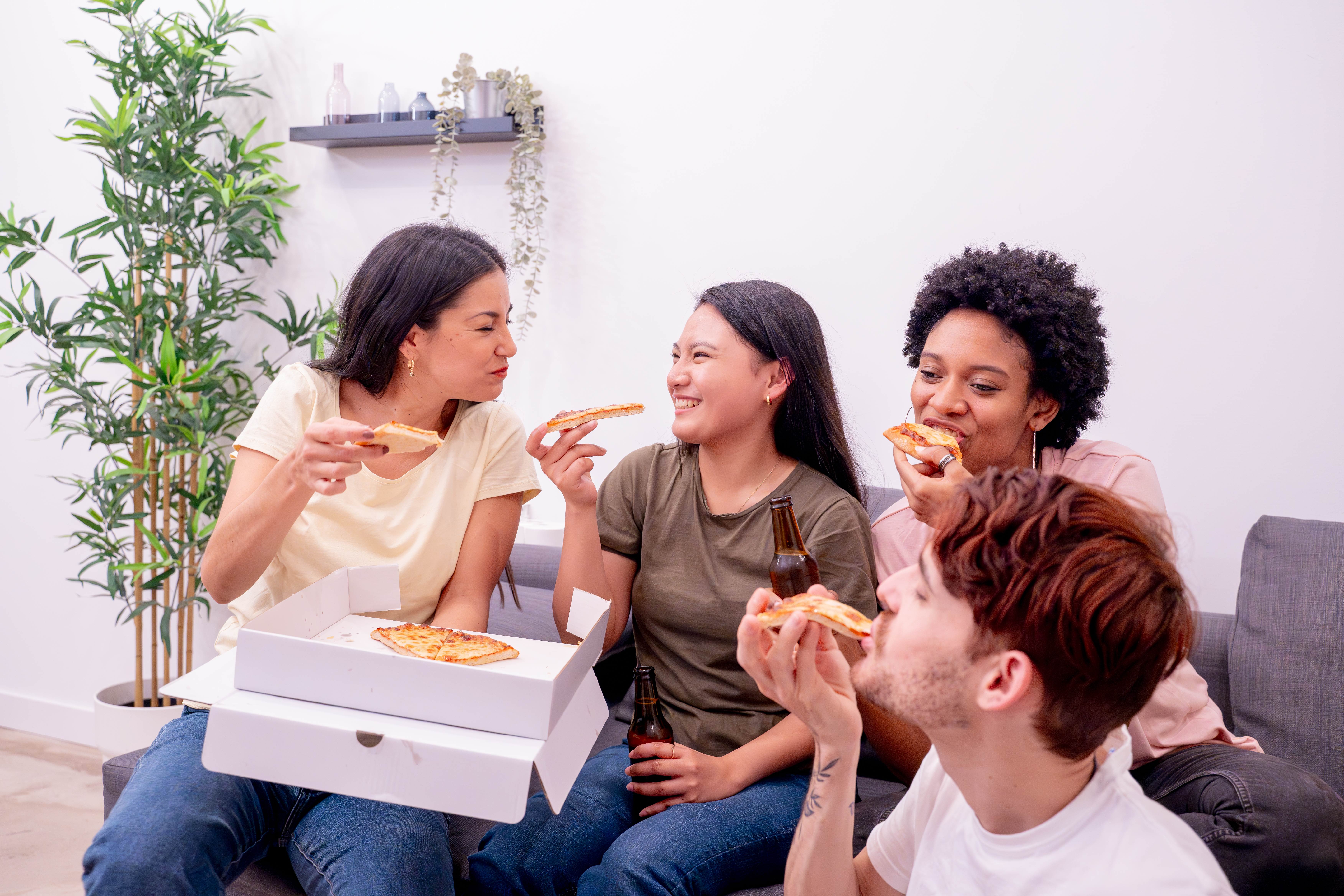 A group of friends sitting together on a couch, enjoying pizza A group of friends sitting together on a couch, enjoying pizza from a catering box and drinks, laughing and sharing a fun moment. Perfect example of pizza catering for casual gatherings.
