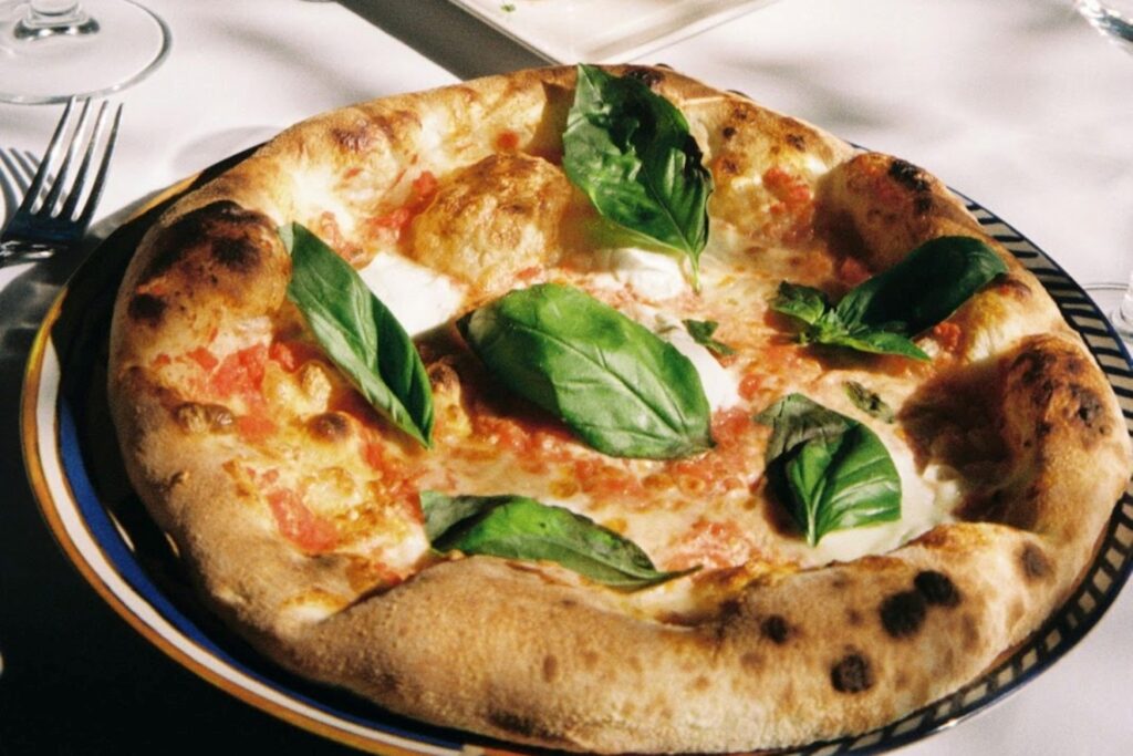 Margherita pizza topped with fresh basil leaves, melted mozzarella, and crushed tomatoes on a wood-fired crust.