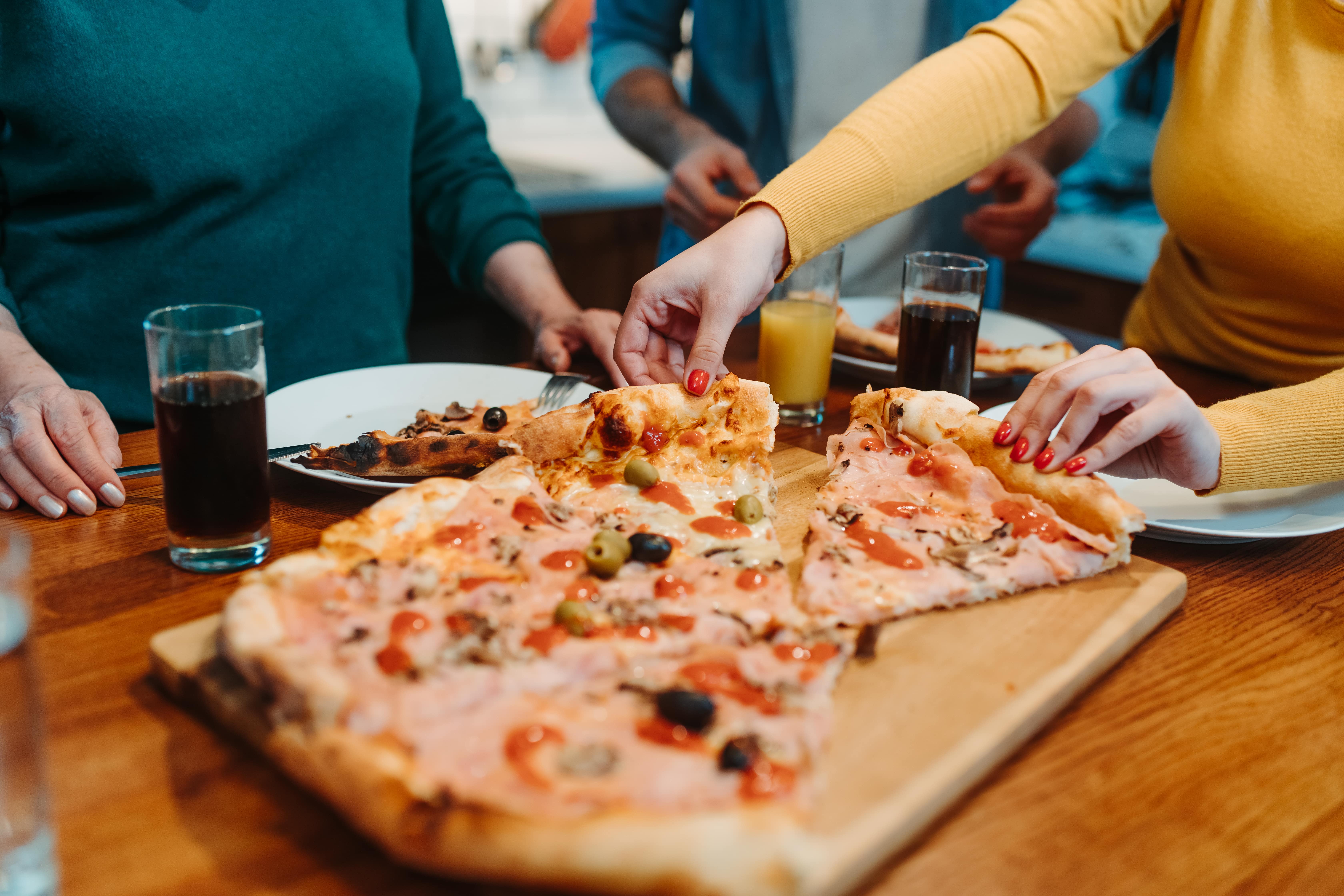 A group of people gathered around a table sharing a pizza A group of people gathered around a table, sharing a large pizza. There are drinks and plates on the table, suggesting a casual and enjoyable meal.