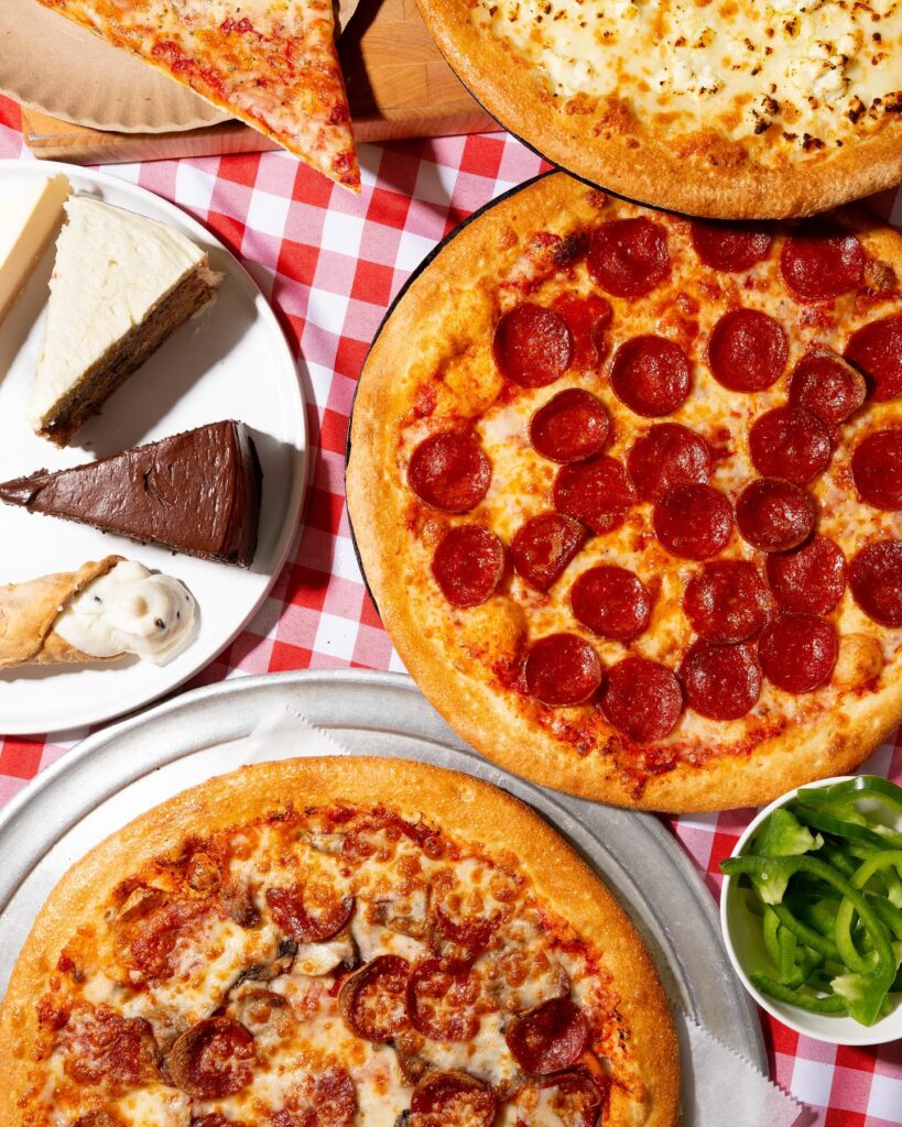 Pepperoni and cheese pizzas with desserts and sides laid out for a full spread from Manny & Olga’s.