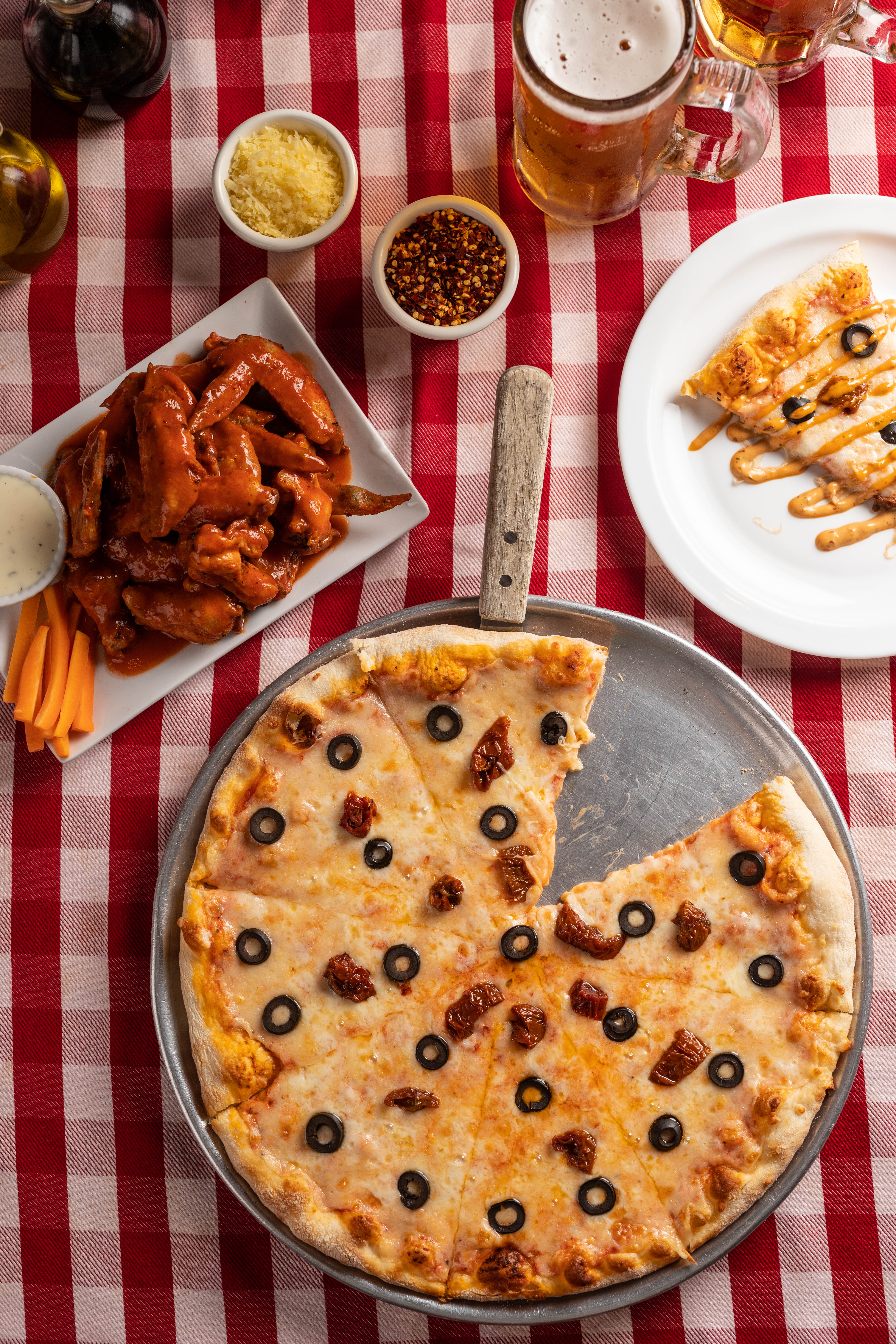 Pepperoni pizza served with buffalo wings and a glass of soda on a wooden table.