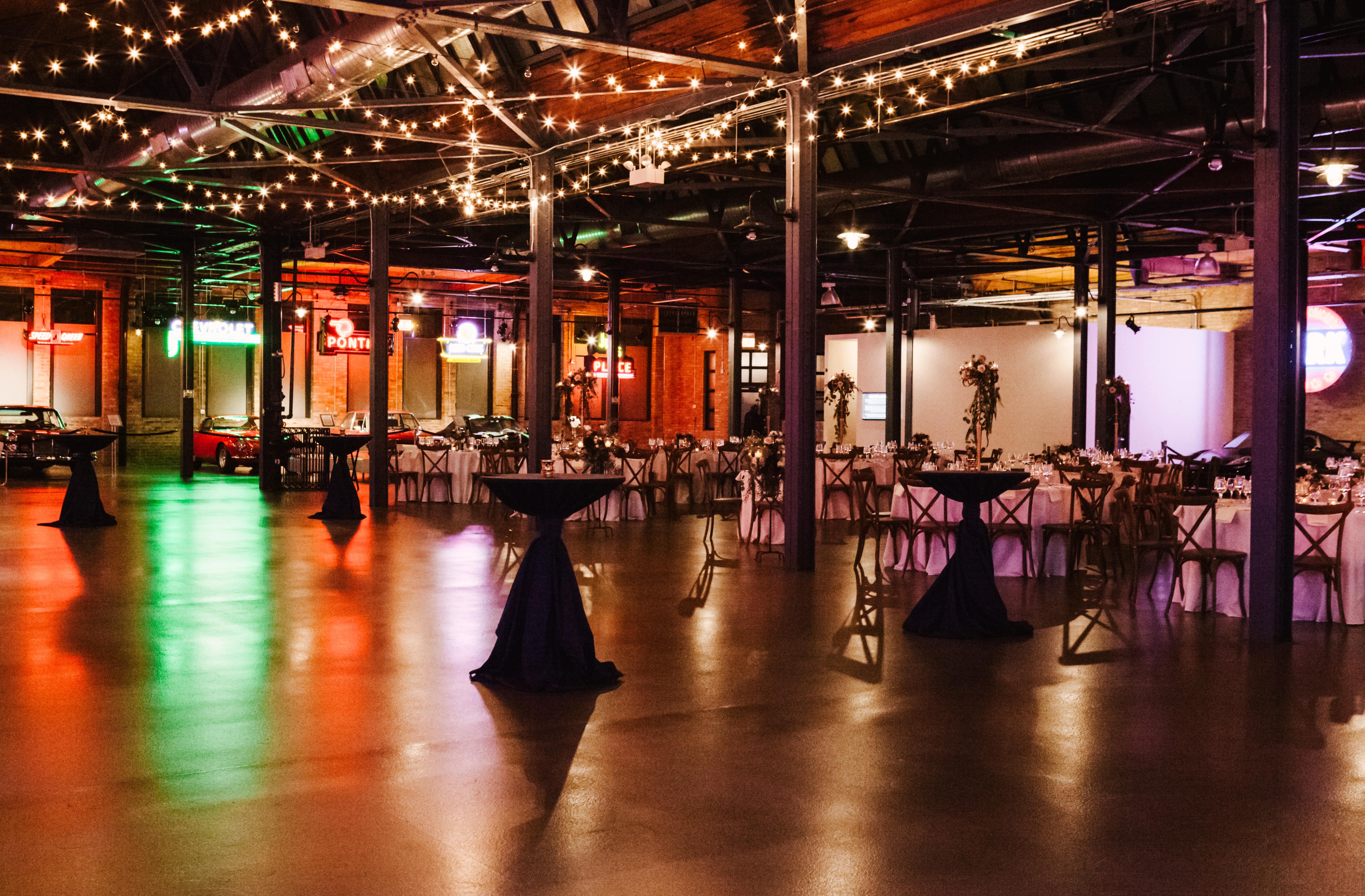 A large, industrial space with high ceilings A large, industrial space with high ceilings and exposed brick walls, decorated with tables and chairs for an event.