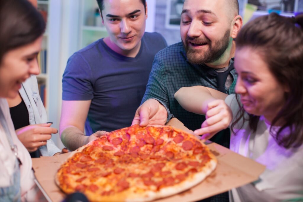 A group of friends enjoying Manny & Olga’s pizza at a football game party.