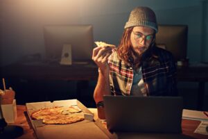 Man eating pizza while working on a laptop late at night.