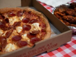 Pepperoni pizza and wings from Manny and Olga's on a red checkered tablecloth.