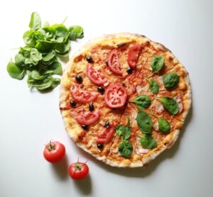 Flatlay shot of a veggie pizza with tomato and basil leaf toppings.