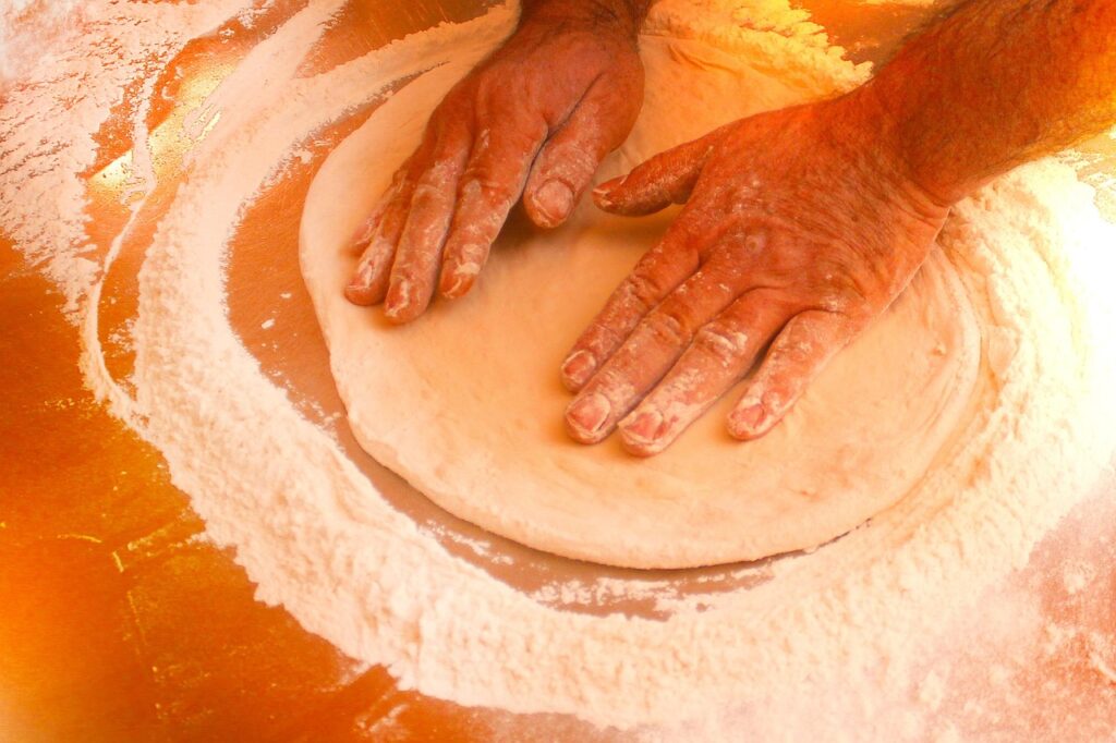 A person prepares the base dough for a pizza.