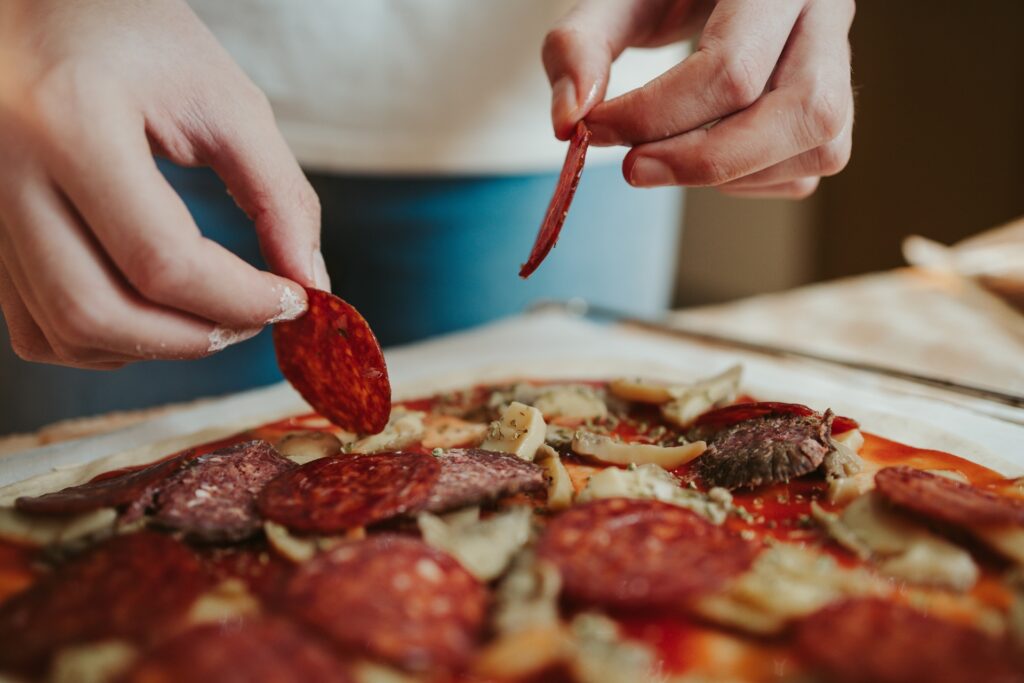 Hand putting pepperoni slices on a pizza.