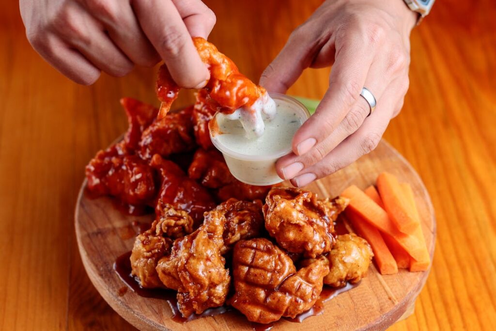 Hand dipping crispy chicken wings into ranch sauce with carrot sticks.