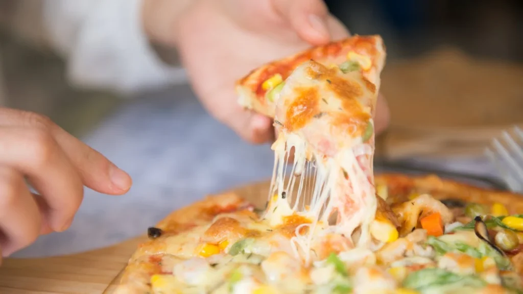 Hands holding a hot, cheesy pizza slice with gooey toppings, perfect for creative leftover pizza recipes.