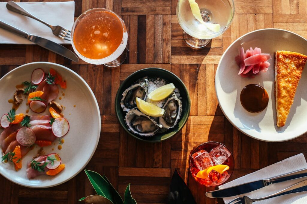 A table set with Greek-inspired dishes, including fresh oysters with lemon, pickled vegetables, and a slice of savory pastry.
