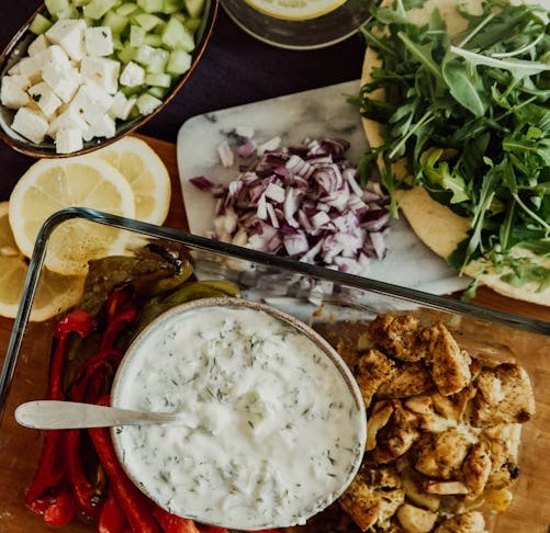 Greek ingredients for a Gyro, including grilled chicken, tzatziki, vegetables, pita, and fresh herbs.