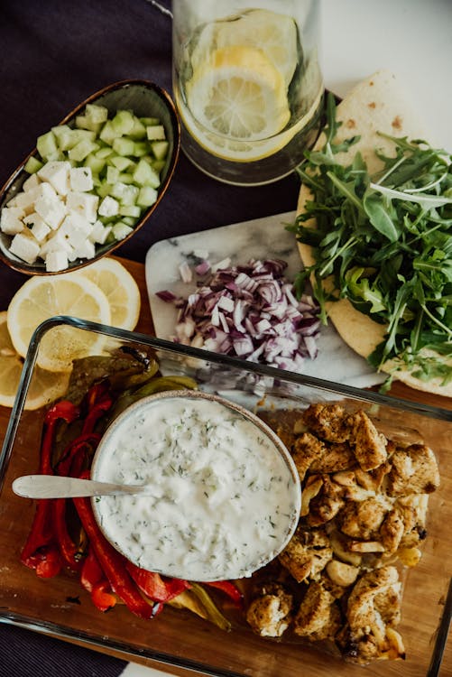 Greek ingredients for a Gyro, including grilled chicken, tzatziki, vegetables, pita, and fresh herbs.
