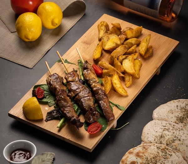 Flame-grilled Chicken Souvlaki skewers with potato wedges, fresh bread, and a glass of wine at Manny & Olga’s.