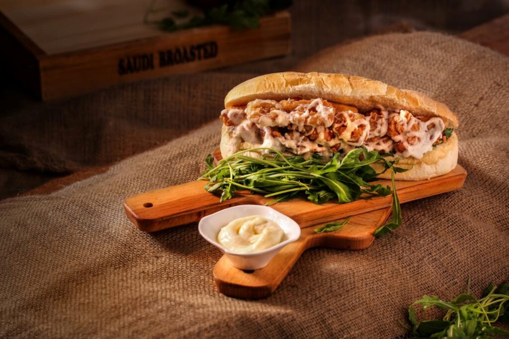 Close-up shot of a filling-rich sub sandwich with garnish and a dip.