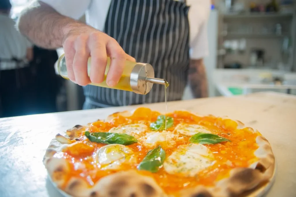 A chef drizzles olive oil over a freshly made pizza with mozzarella and basil leaves for extra flavor.
