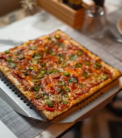 A square pizza topped with pepperoni, mushrooms, and jalapeños on a perforated pan.