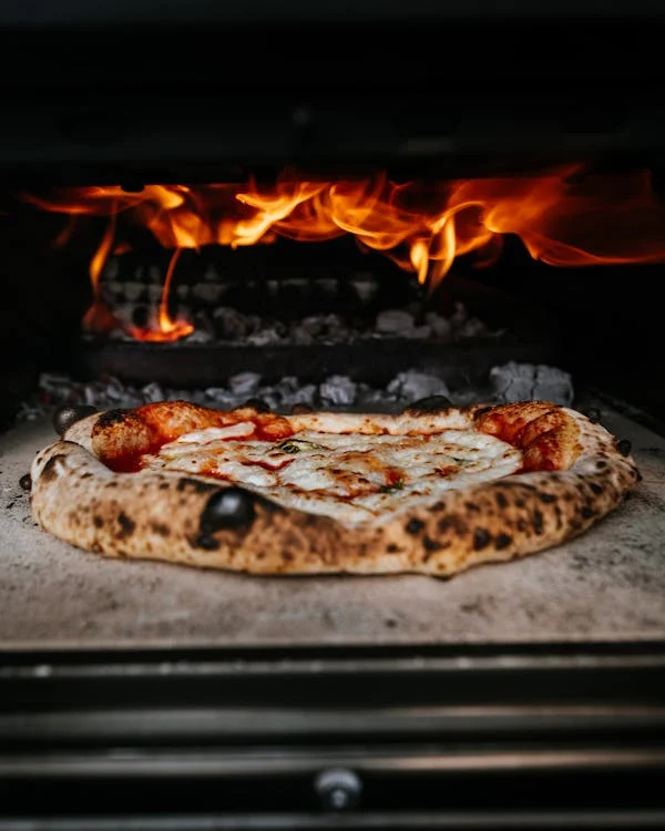 Neapolitan pizza baking in a wood-fired oven, highlighting fresh crust and melted cheese ideal for next-day recipes.