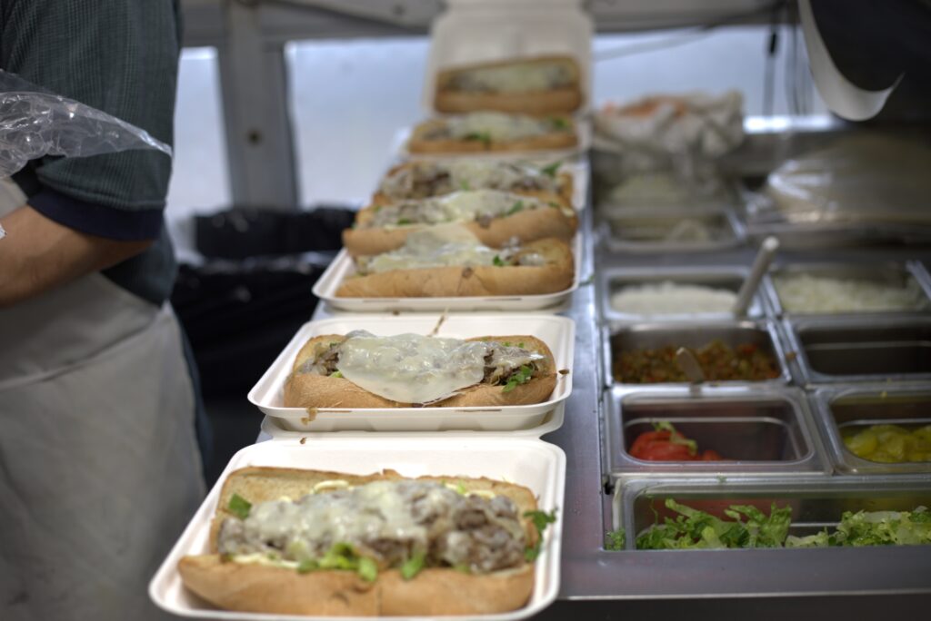 A close-up of several Philly cheesesteak subs with melted cheese and grilled onions from Manny & Olga's.