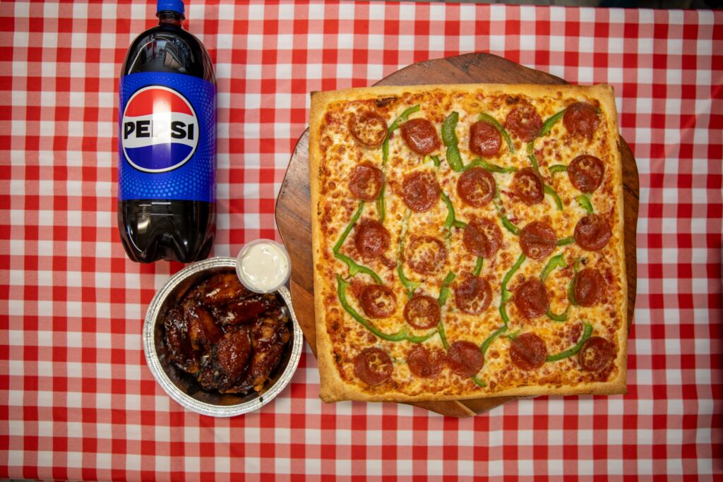 A pepperoni and green pepper pizza, alongside a serving of chicken wings and a Pepsi bottle from Manny & Olga's.