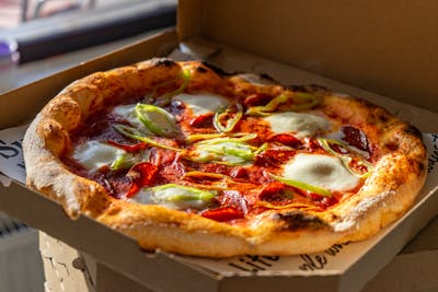 A pizza with pepperoni, mozzarella, and green onions in a pizza box, showing a golden, crispy crust.