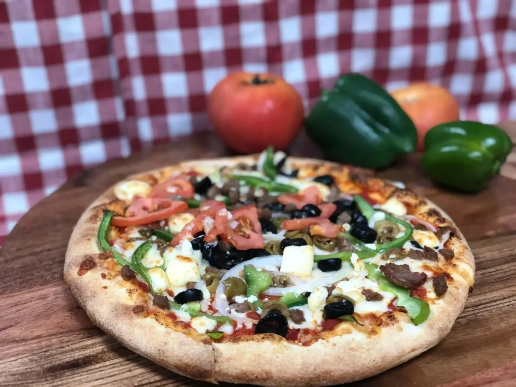Freshly baked pizza at Manny & Olga’s topped with locally sourced tomatoes, green peppers, olives, and melted cheese.