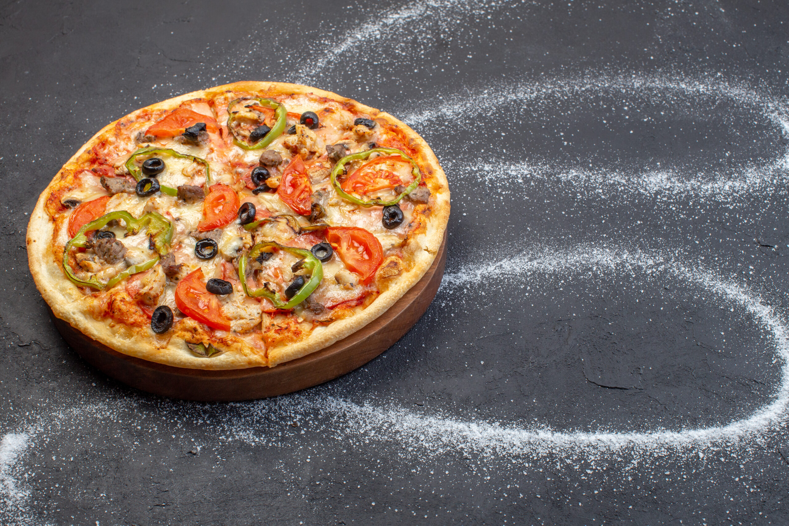 Pizza on a wooden board with olives and peppers, surrounded by flour swirls resembling a galaxy pattern.