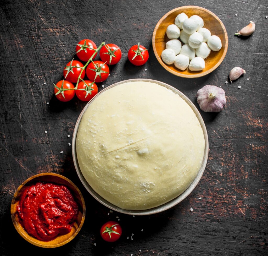 Raw pizza dough topped with tomato paste, mozzarella, and cherry tomatoes before baking.
