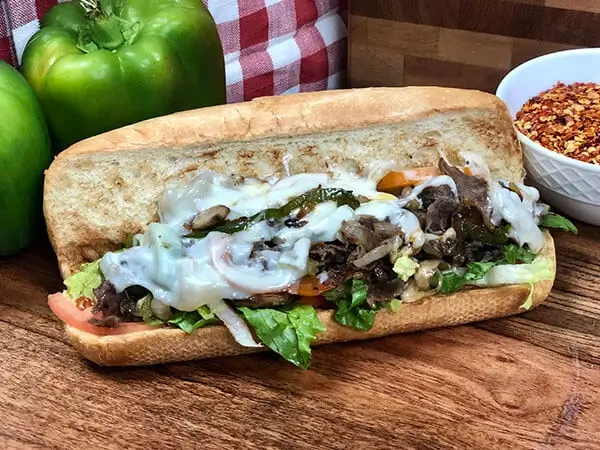 Manny & Olga’s steak and cheese sub with melted cheese, lettuce, and onions on a wooden board.