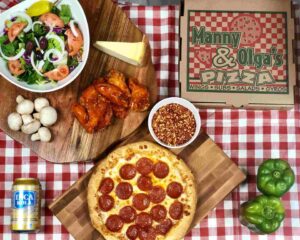 A flat-lay of Manny & Olga’s wings, cheesy pizza, and sides, highlighting their signature D.C. comfort food offerings.