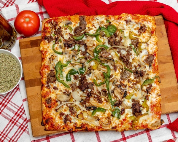 Manny and Olga’s BBQ Chicken Pizza served with oregano on a wooden slab.